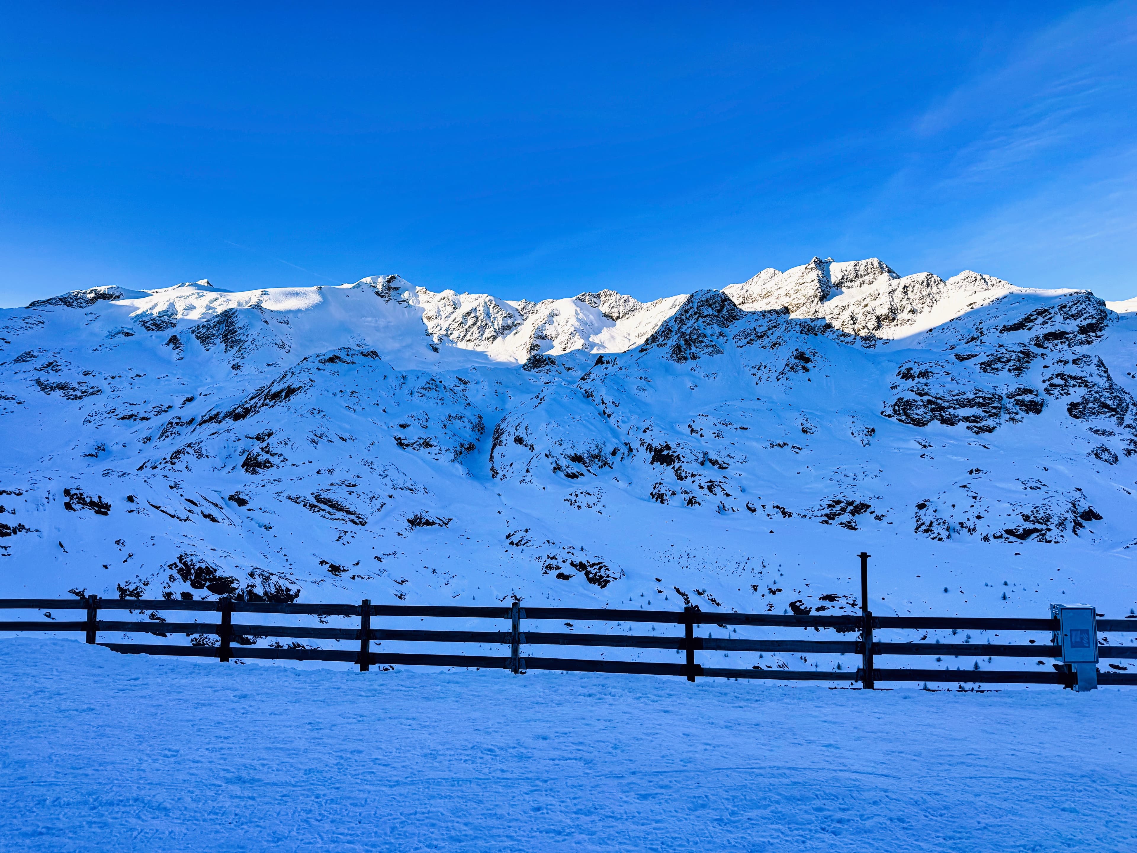 The alpine panorama from above Pizzini — deep blue sky, massive snowy peaks